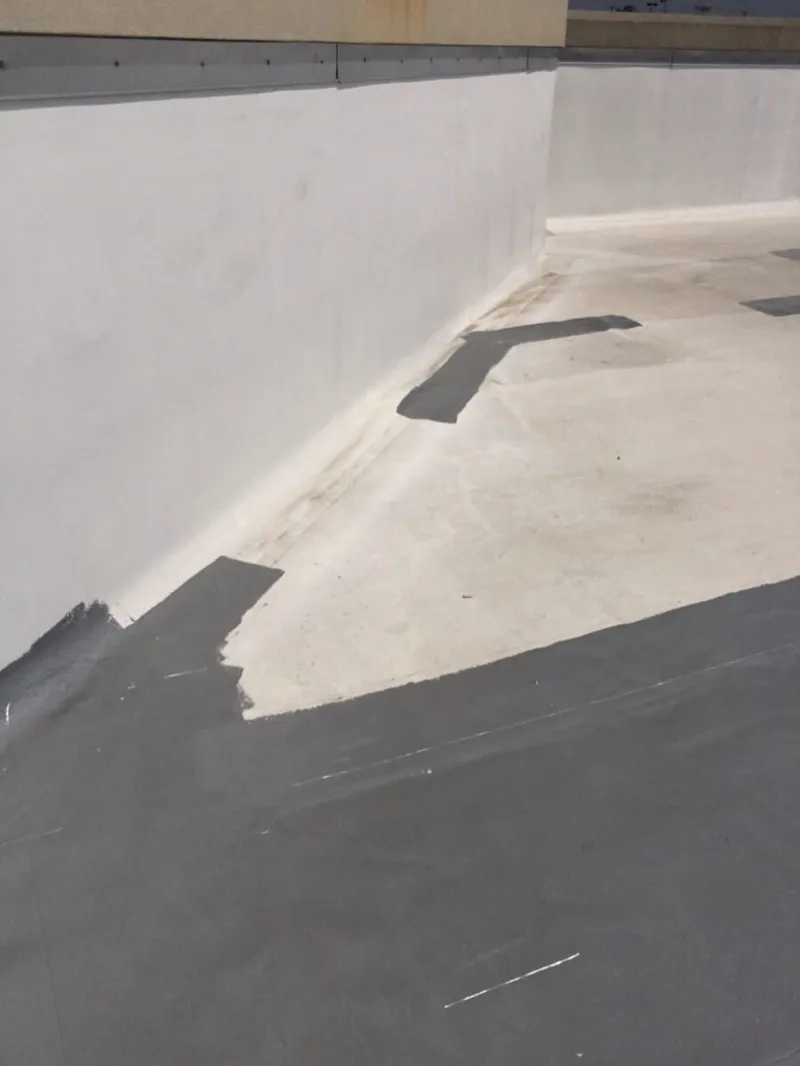Technician applying elastic fluid sealant around a roof penetration pipe base