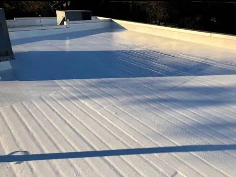 Applying silicone roofing coating to flat roof surface around ventilation pipes